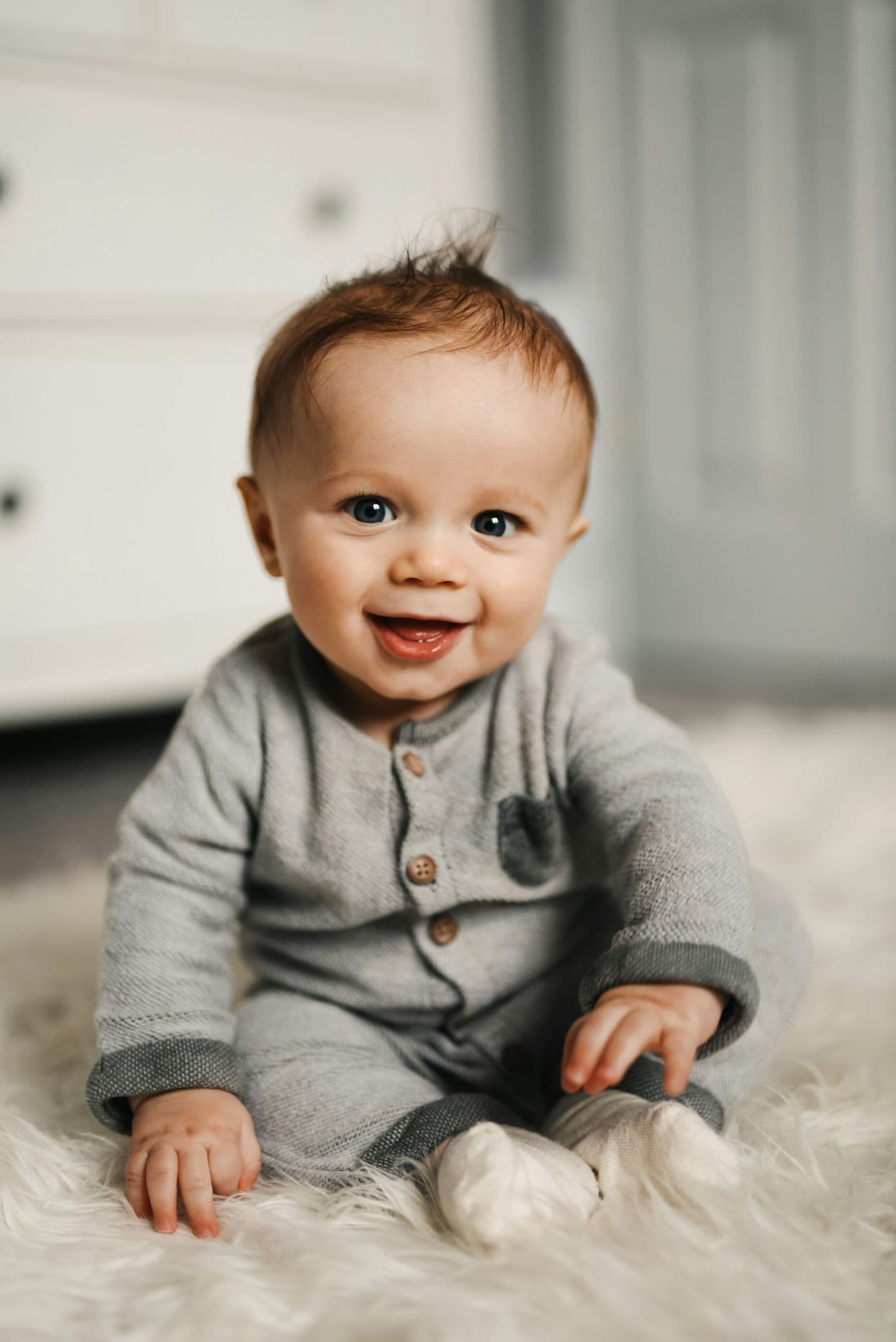 A baby sitting up in a grey knitted romper