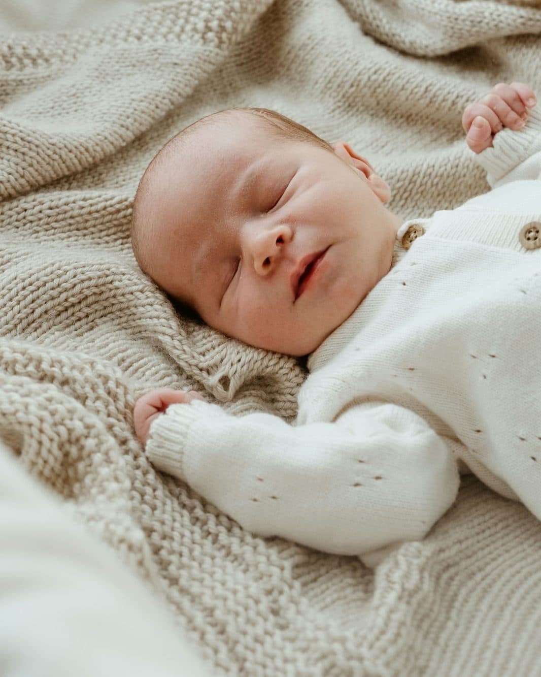 A sleeping newborn resting on a cream knitted blanket